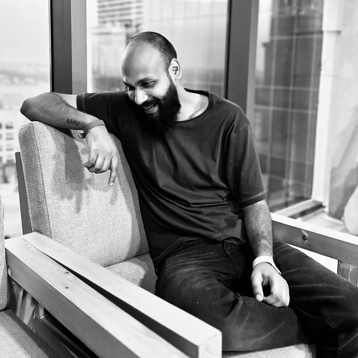 Rameez, smiling, sitting in an armchair by a window